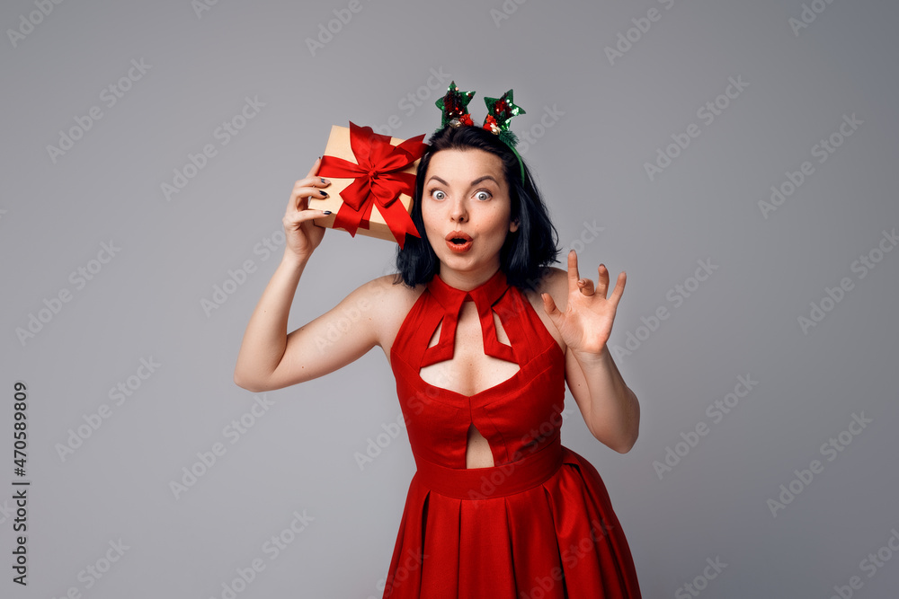 Curious young woman wonder what is inside gift box. Smiling happy girl in red dress on gray background. Holidays, celebration and lifestyle concept Curious young woman wonder what is inside gift box. Smiling happy girl in red dress on gray background. Holidays, celebration and lifestyle concept