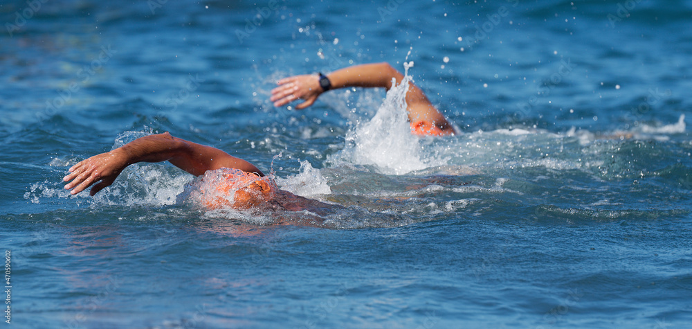 Two swimmers swimming crawl in blue sea, training for triathlon
