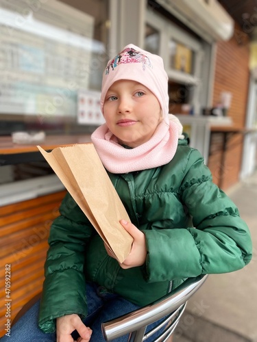 Little girl in green jacket with paper bag.