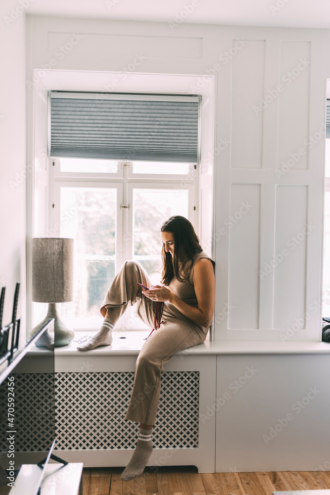 Woman using smart phone sitting on window sill at home Woman using smart phone sitting on window sill at home