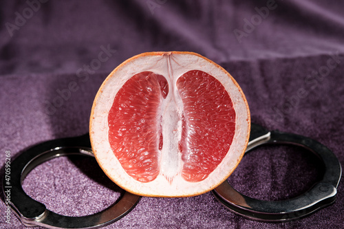 Half grapefruit and handcuffs close-up on a purple background. The concept of protecting virginity, sexual inviolability. Vagina symbol.