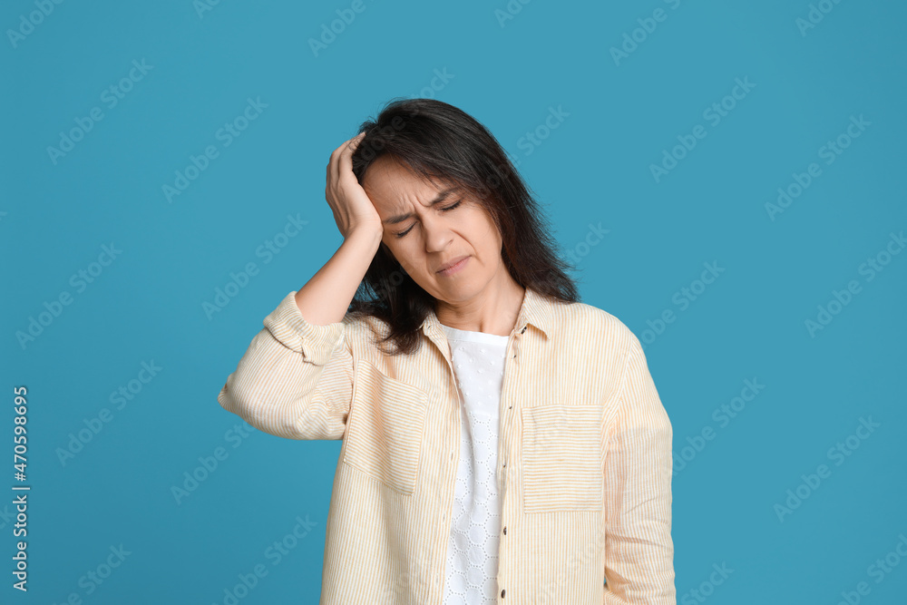 Mature woman suffering from headache on light blue background Mature woman suffering from headache on light blue background