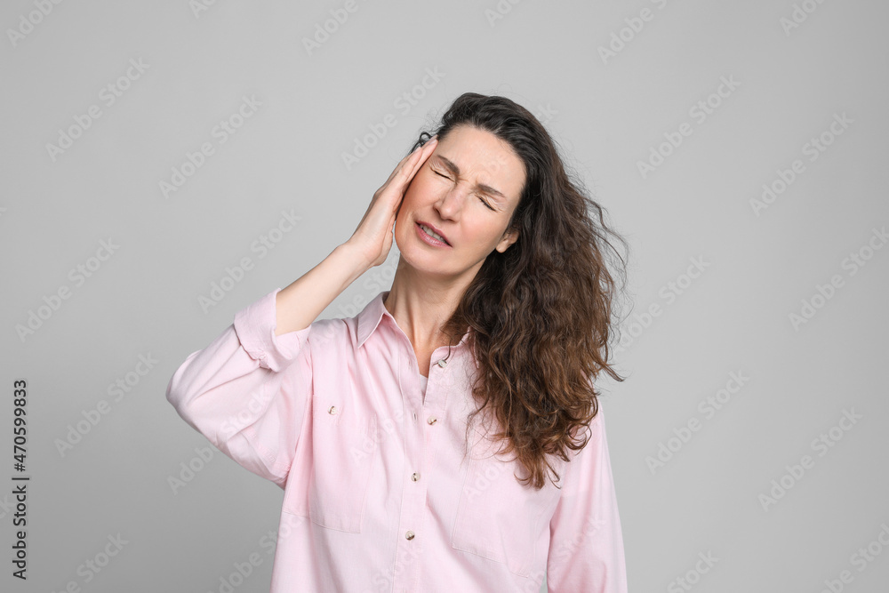 Mature woman suffering from headache on light grey background Mature woman suffering from headache on light grey background