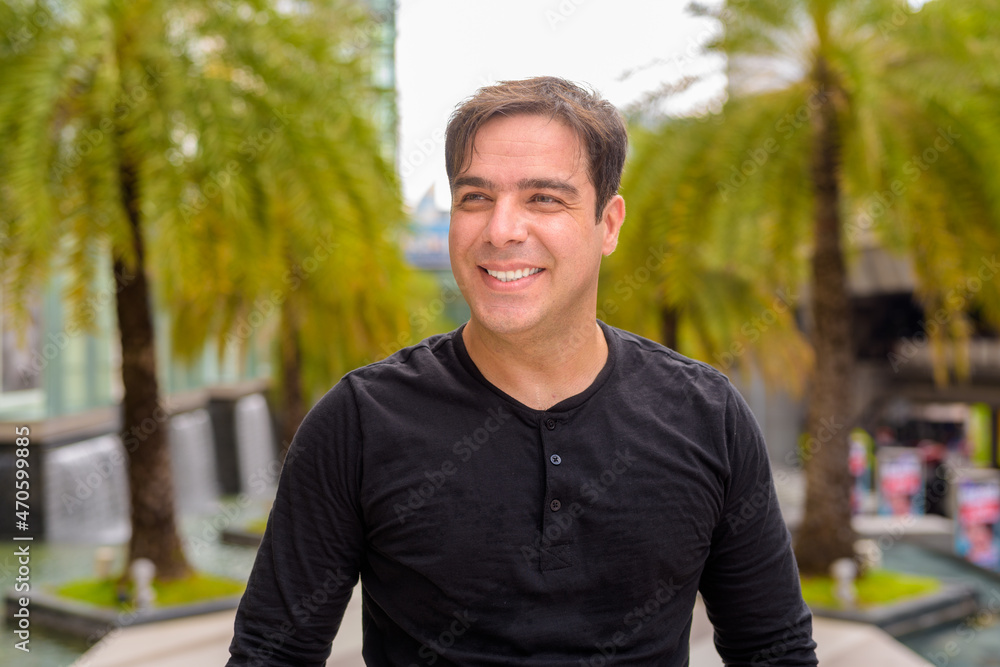 Portrait of handsome Persian man outdoors smiling and thinking in city during summer Portrait of handsome Persian man outdoors smiling and thinking in city during summer