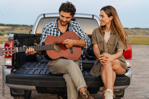 Young white couple playing guitar while sitting in trunk during journey