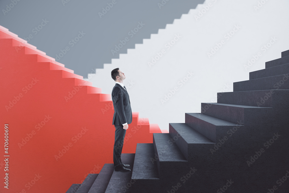 Attractive young european businessman standing on red and concrete staircase with mock up place. Success, finance and career growth concept.