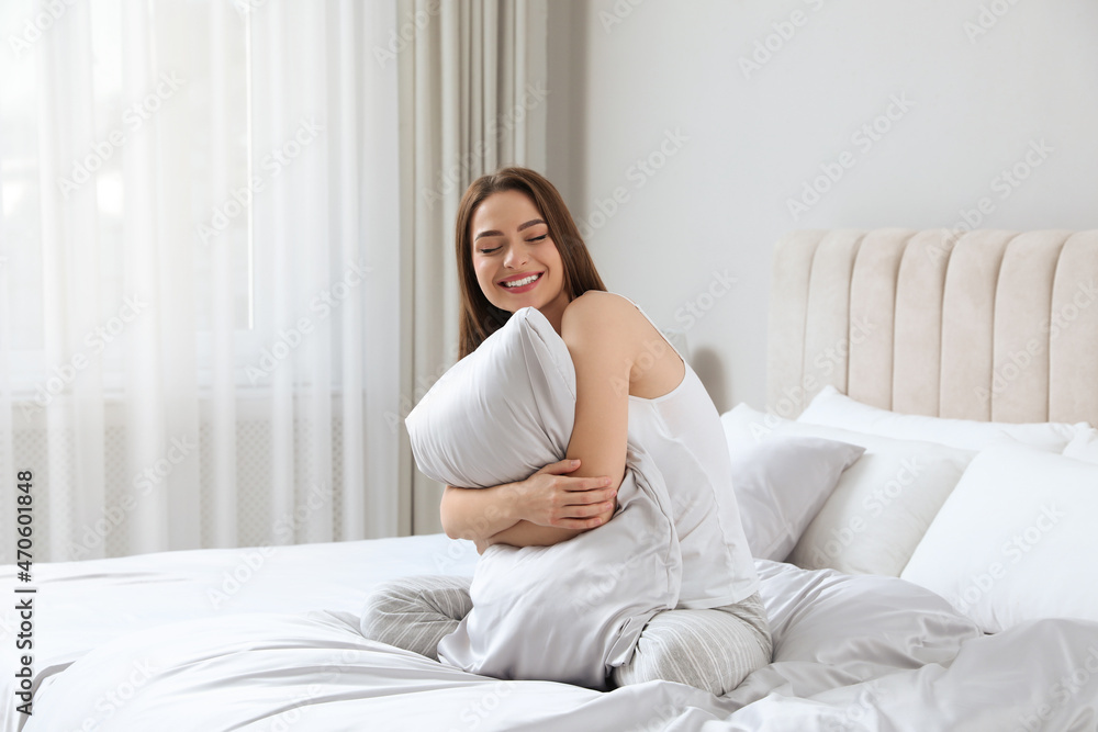 Young woman hugging pillow on comfortable bed with silky linens Young woman hugging pillow on comfortable bed with silky linens