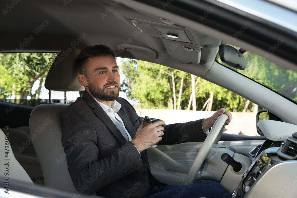 Handsome young driver with cup of drink sitting in modern car