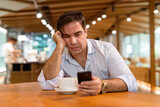 Bored Persian man sitting at coffee shop while using mobile phone