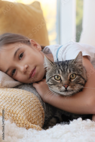 Cute little girl with her cat at home, closeup. Childhood pet