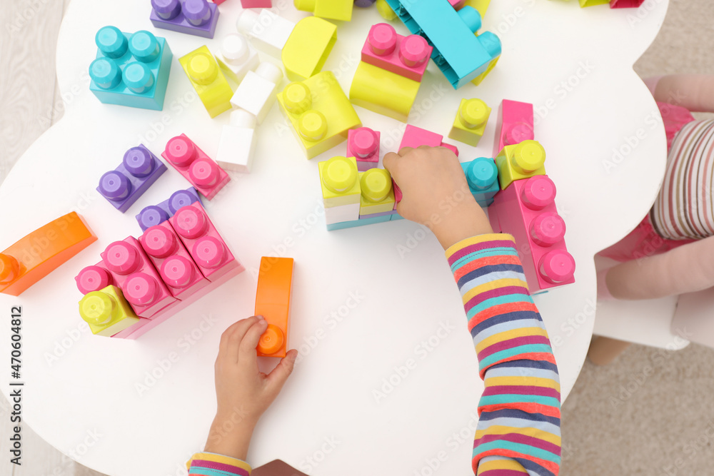 Cute little girl playing with colorful building blocks at table indoors, top view Cute little girl playing with colorful building blocks at table indoors, top view