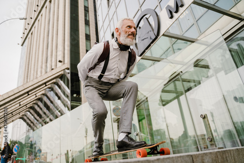 Grey mature man smiling while skateboarding at city street