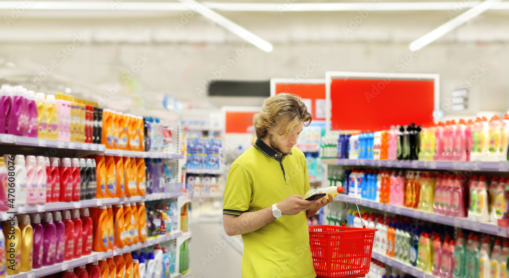 Man shopping in supermarket reading product information.(diapers,detergent)
