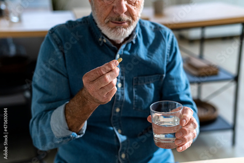 Senior man holding glass of water taking medicine at home