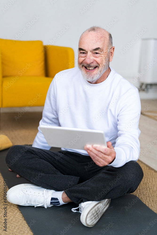 Smiling senior man using tablet PC on exercise mat at home Smiling senior man using tablet PC on exercise mat at home