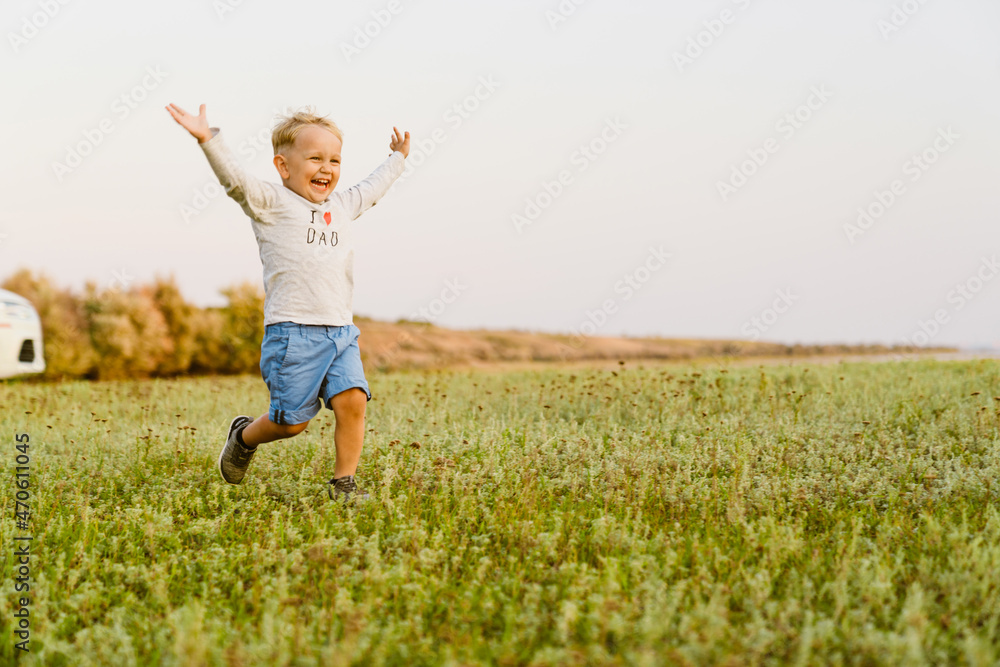Blonde white boy smiling while running with hands up on field Blonde white boy smiling while running with hands up on field