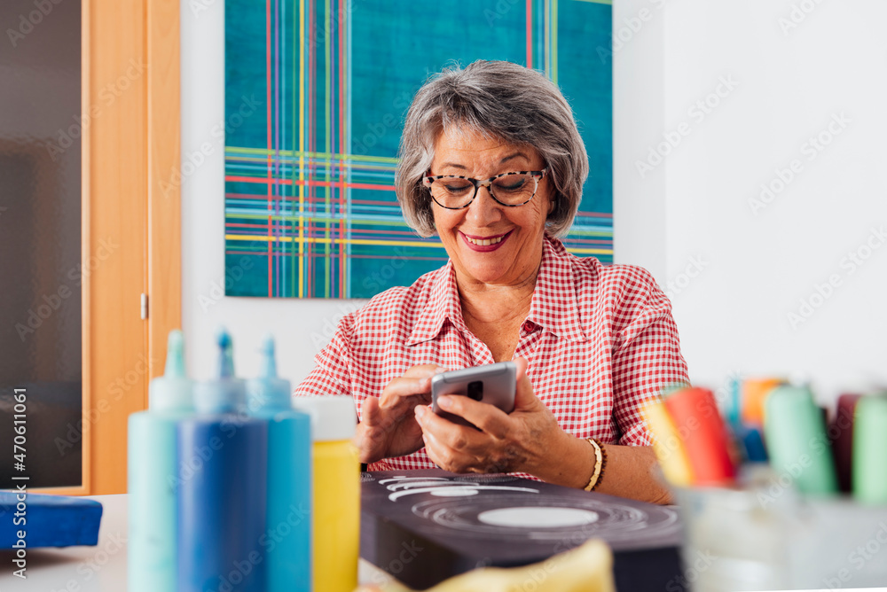 Smiling woman photographing painting through smart phone at home Smiling woman photographing painting through smart phone at home