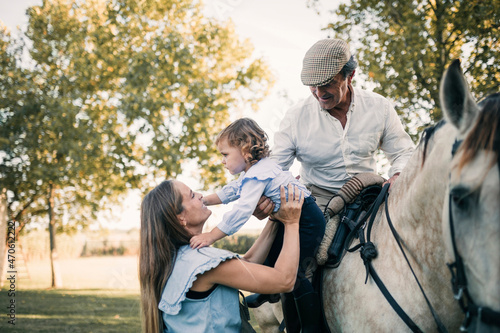 Mother carrying daughter while senior man sitting on horse photo
