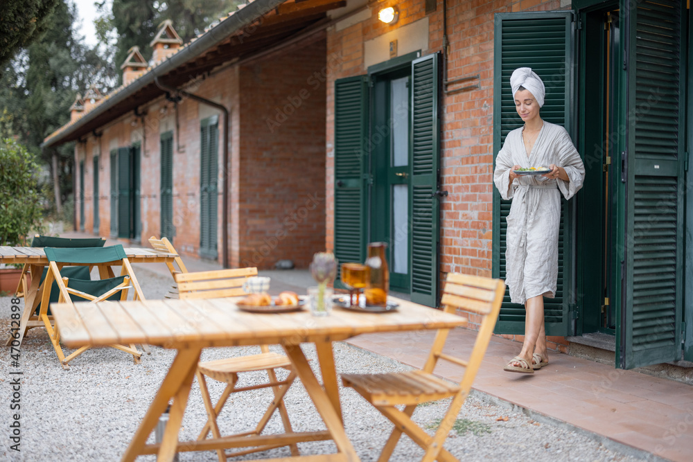Fototapeta premium Woman carrying food to table for breakfast during resting in hotel at morning time. Concept of weekend, tourism and vacation. Young caucasian woman wearing bathrobe and wrapped bath towel on head
