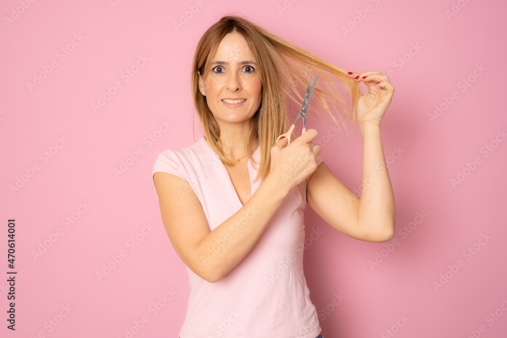 Young beautiful woman cutting her hair tips with scissors isolated over pink background. Young beautiful woman cutting her hair tips with scissors isolated over pink background.