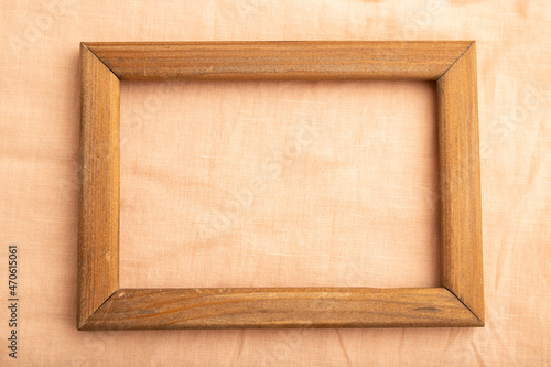 Wooden frame on smooth orange linen tissue. Top view, natural textile background.