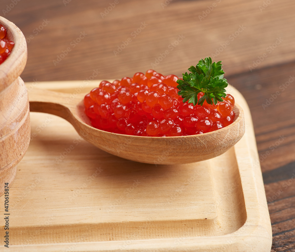 red caviar of pink salmon lies in a wooden spoon on a brown wooden table red caviar of pink salmon lies in a wooden spoon on a brown wooden table