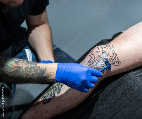 Tattoo artist shaves leg skin area before painting new tattoo tiger head style