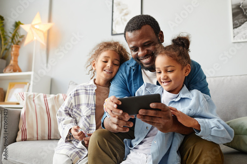 Portrait of happy African-American father using smartphone with two little girls, copy space