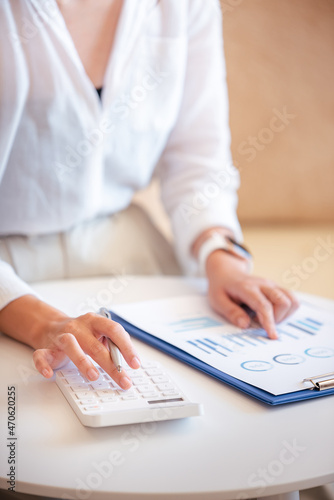 A young woman's hand presses a calculator to determine and summarize the cost of mortgage home loans for refinancing plans, lifestyle concepts.