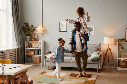 Full length portrait of two African-American girls playing with father in cozy home interior, copy space