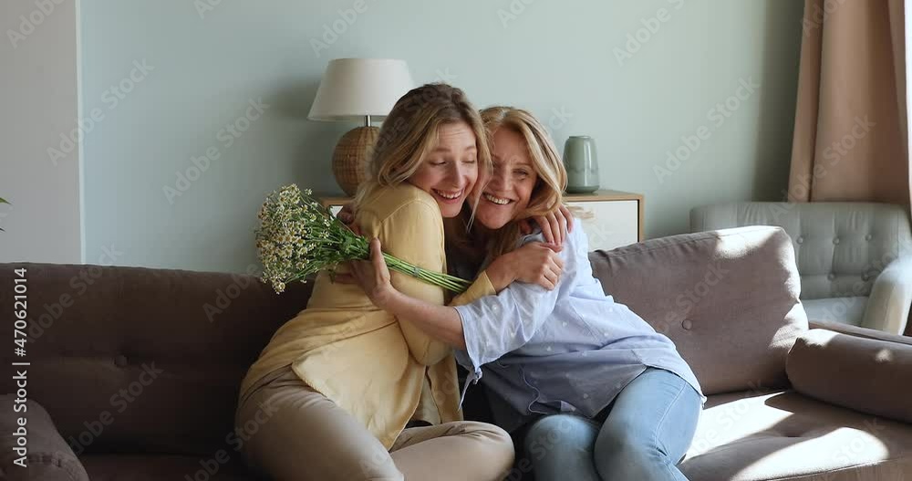Caring daughter give bunch of spring flowers to beloved older mother embrace dear mom express love care gratitude. Smiling young female present bouquet of chamomile to aged mum congratulate on holiday Caring daughter give bunch of spring flowers to beloved older mother embrace dear mom express love care gratitude. Smiling young female present bouquet of chamomile to aged mum congratulate on holiday