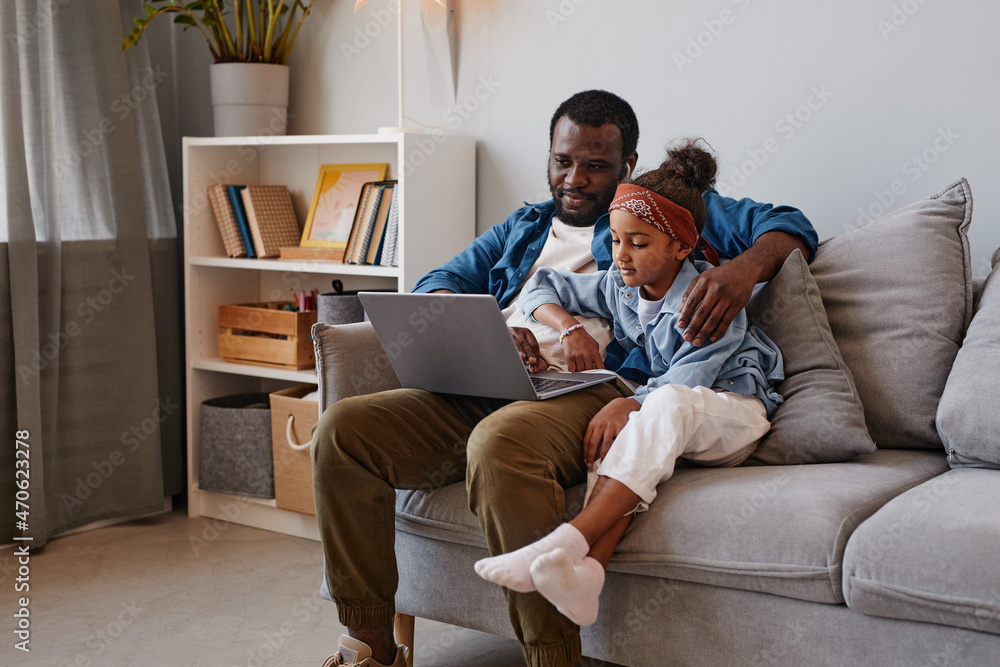 Portrait of happy African-American father using laptop with cute daughter, copy space