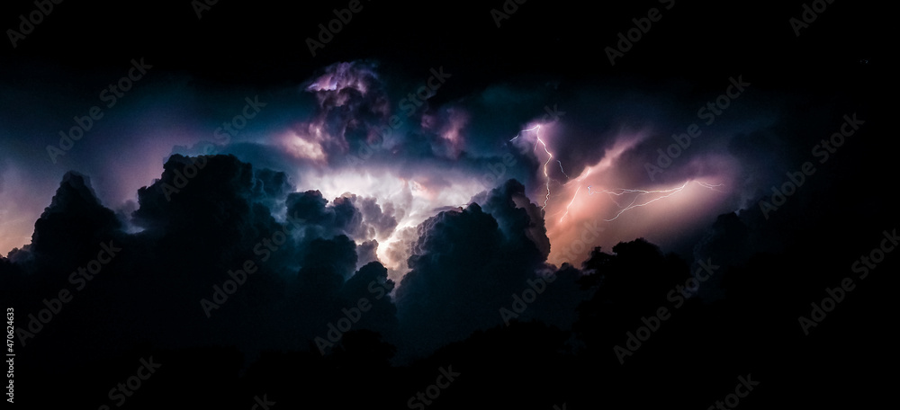 Flashes of lightning and clouds during thunderstorms at night. Panoramic photo.