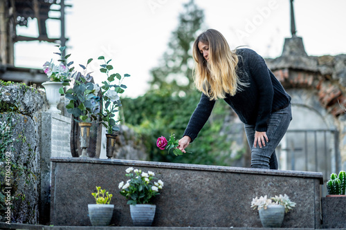 Blond woman putting flower on grave at cemetery photo