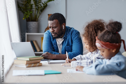 Portrait of caring father doing homework with two little girls in online school at home, copy space