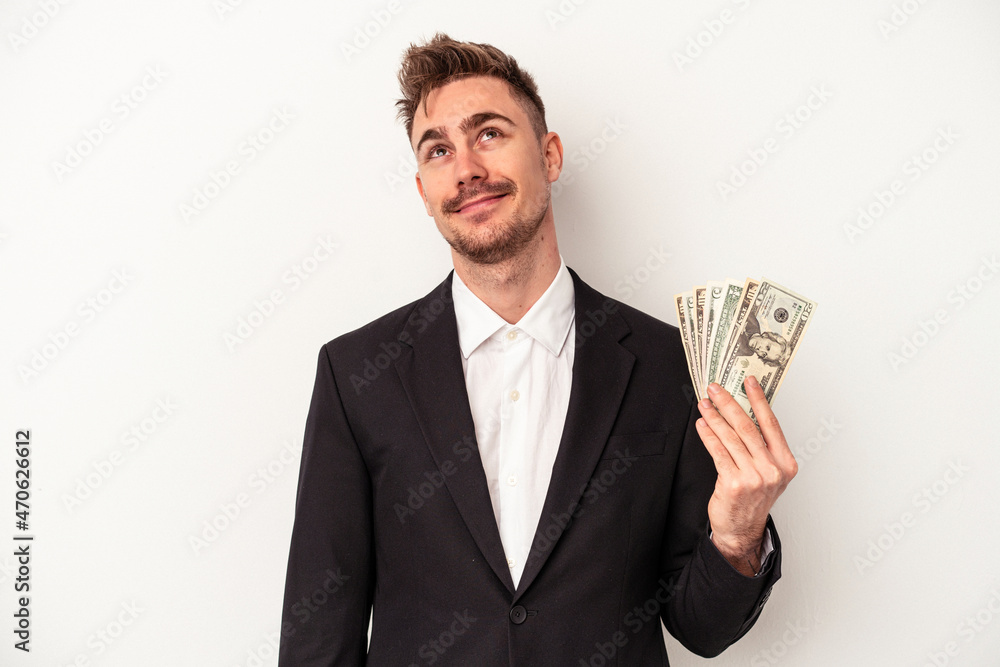 Young caucasian business man holding bank notes isolated on white background dreaming of achieving goals and purposes Young caucasian business man holding bank notes isolated on white background dreaming of achieving goals and purposes