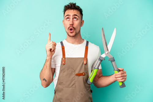 Young gardener caucasian man holding a scissors isolated on blue background pointing upside with opened mouth.