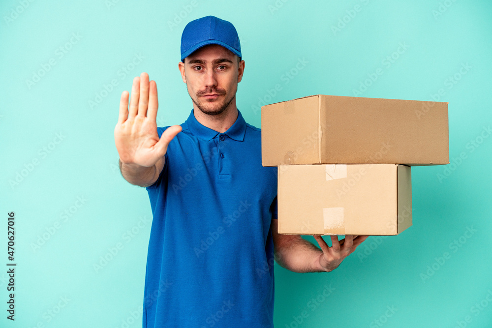 Young delivery caucasian man isolated on blue background standing with outstretched hand showing stop sign, preventing you. Young delivery caucasian man isolated on blue background standing with outstretched hand showing stop sign, preventing you.