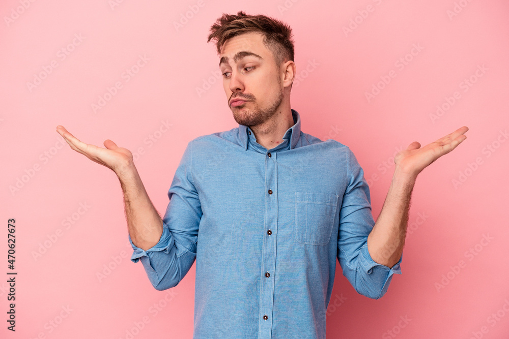 Young caucasian man isolated on pink background confused and doubtful shrugging shoulders to hold a copy space.