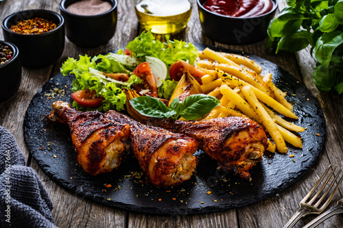 Barbecue chicken drumsticks with chips and greens on wooden table 