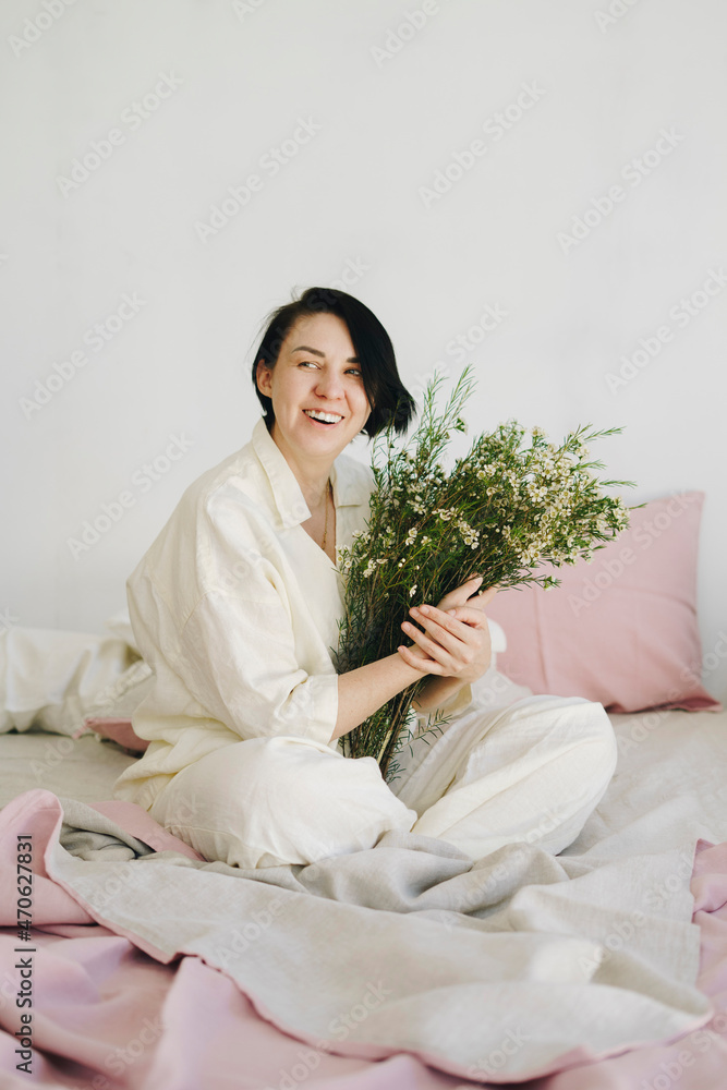 Cheerful woman with flower bouquet sitting on bed at new home Cheerful woman with flower bouquet sitting on bed at new home
