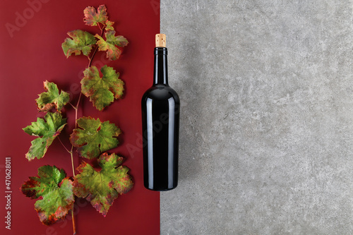 Top view of bottle of red wine with green fall grapes leaves a on red and grey stone geometric background, concept of modern red wine flat lay background, copy space