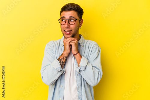 Young caucasian man with tattoos isolated on yellow background praying for luck, amazed and opening mouth looking to front.