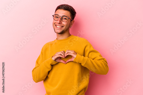 Young caucasian man with tattoos isolated on yellow background smiling and showing a heart shape with hands.