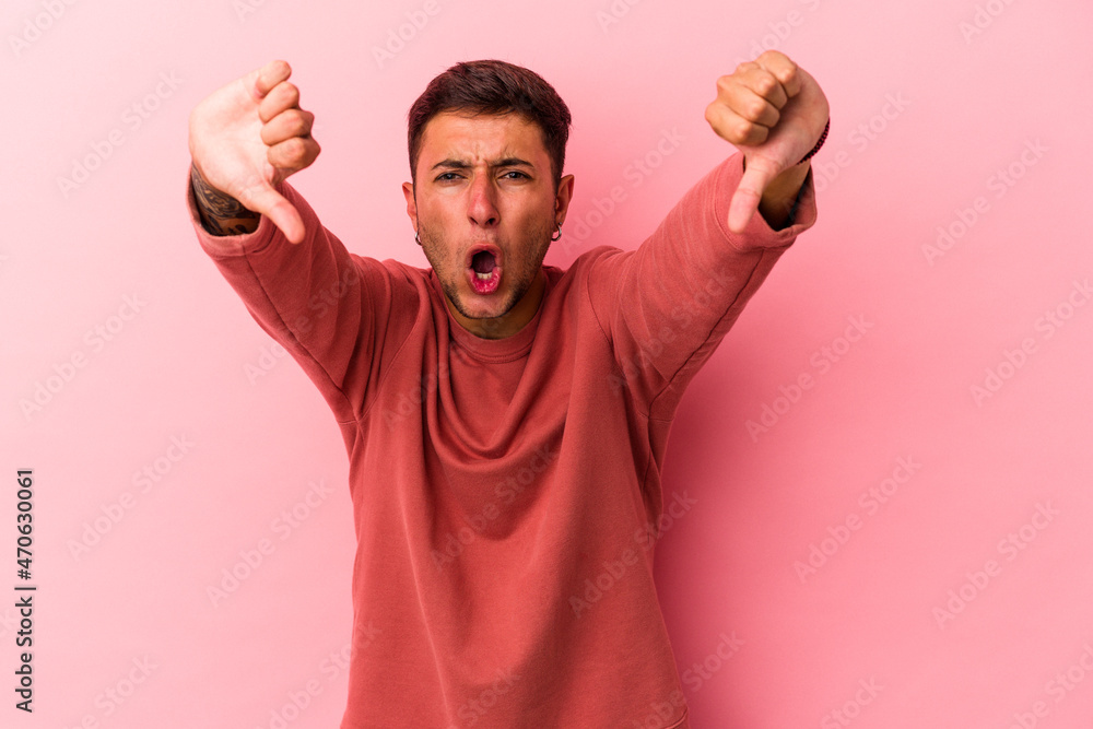 Young caucasian man with tattoos isolated on yellow background  showing thumb down and expressing dislike.