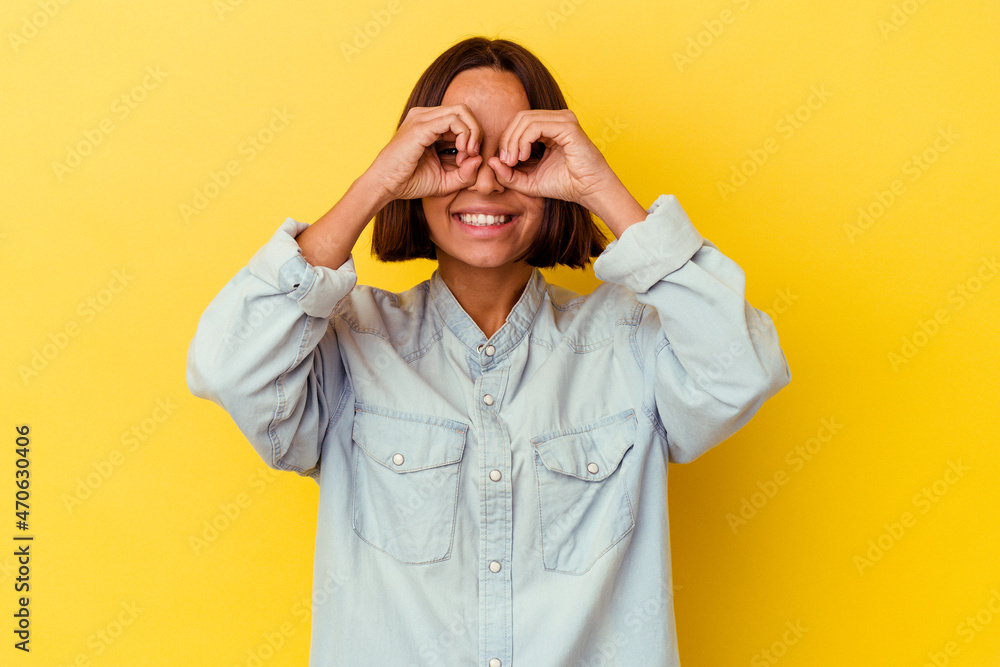 Young mixed race woman isolated on yellow background showing okay sign over eyes Young mixed race woman isolated on yellow background showing okay sign over eyes
