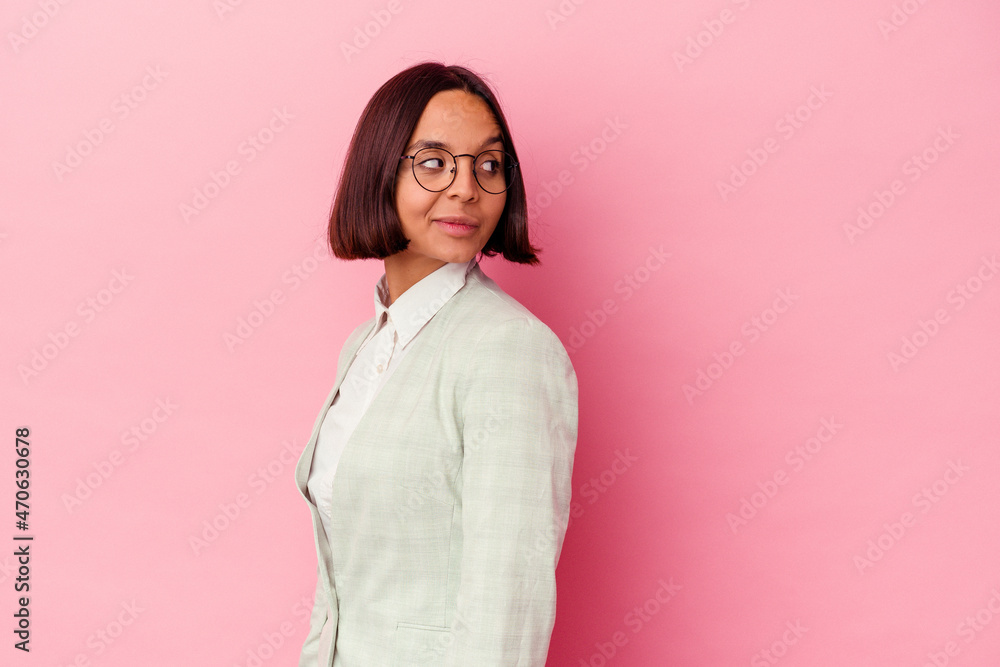 Fototapeta premium Young mixed race woman wearing a green suit isolated on pink background looks aside smiling, cheerful and pleasant.