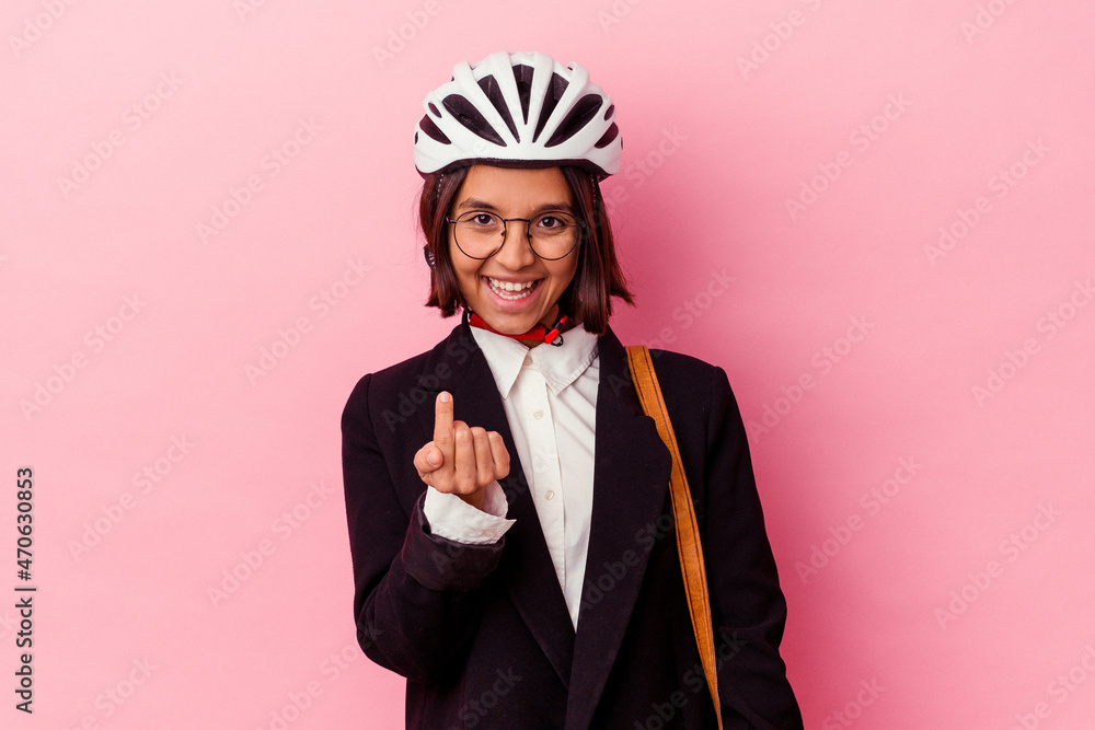 Young business mixed race woman wearing a bike helmet isolated on pink background pointing with finger at you as if inviting come closer. Young business mixed race woman wearing a bike helmet isolated on pink background pointing with finger at you as if inviting come closer.