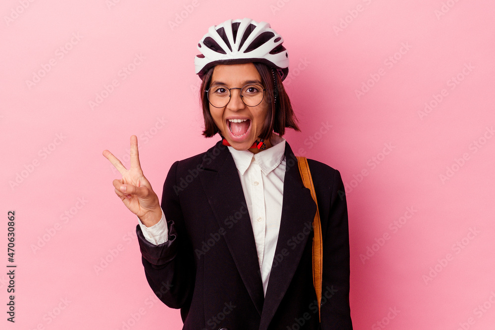 Young business mixed race woman wearing a bike helmet isolated on pink background joyful and carefree showing a peace symbol with fingers. Young business mixed race woman wearing a bike helmet isolated on pink background joyful and carefree showing a peace symbol with fingers.