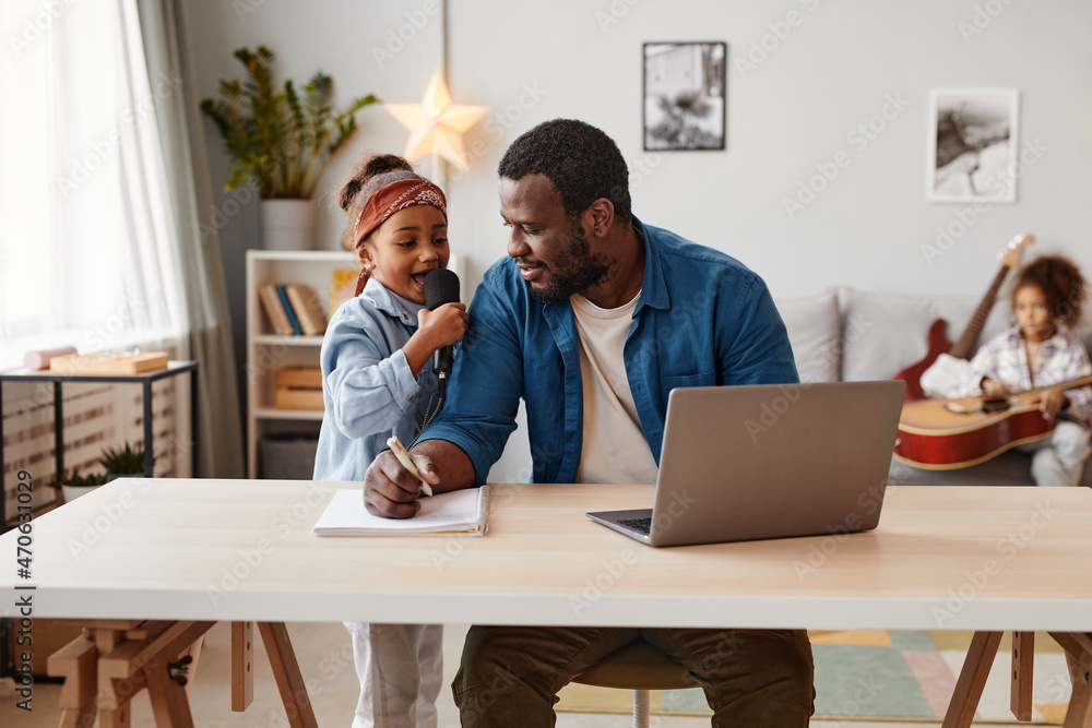 Portrait of modern African-American father using laptop while working at home with kids, copy space Portrait of modern African-American father using laptop while working at home with kids, copy space